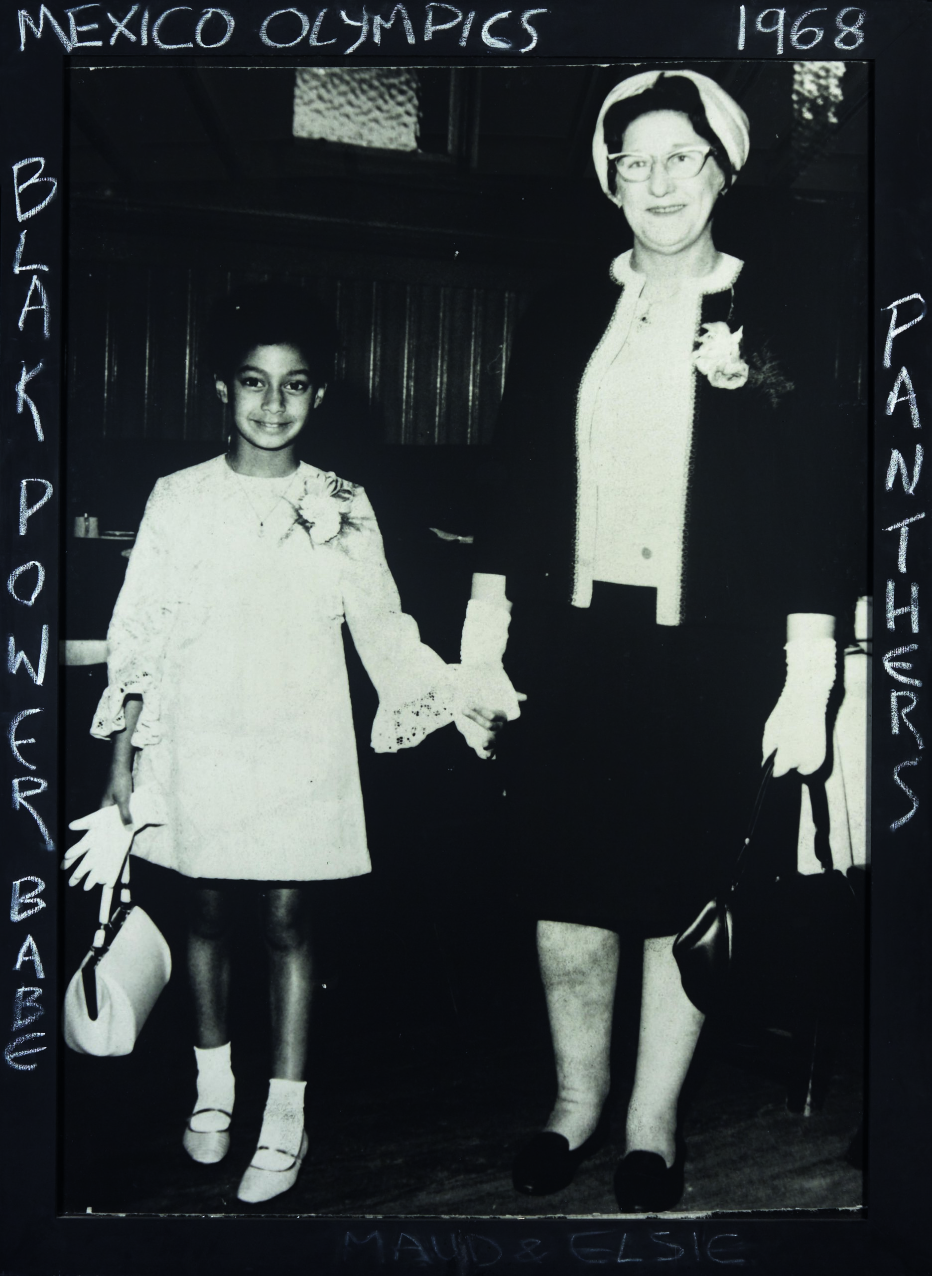 Black and white photograph of a young child holding hands with an older lady. They are both smiling at the camera.